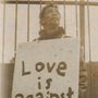 A man holding a sign saying Love is against the grain