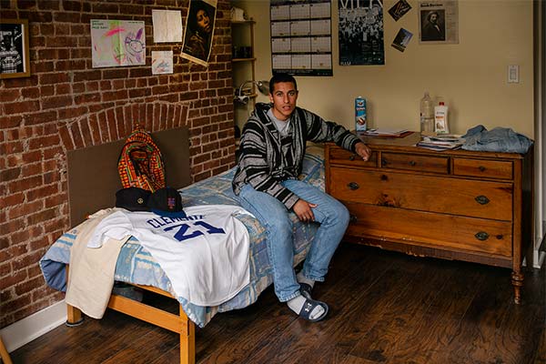 Rubén Ayala sitting on a bed surrounded by mementos of his dad