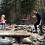 a girl walking across a log over a stream to her dad