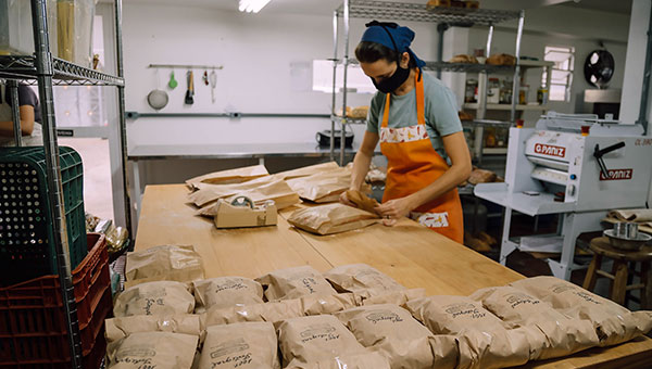 young woman putting bread in brown paper bagss