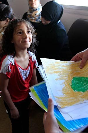 A girl from Syria in a refugee center looks up smiling at a caregiver.