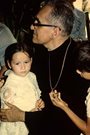 Archbishop Oscar Romero with two children, one of whom is holding his archbishop's cross in his hand and gazing at it.