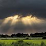 sun breaking through dark clouds over a pasture