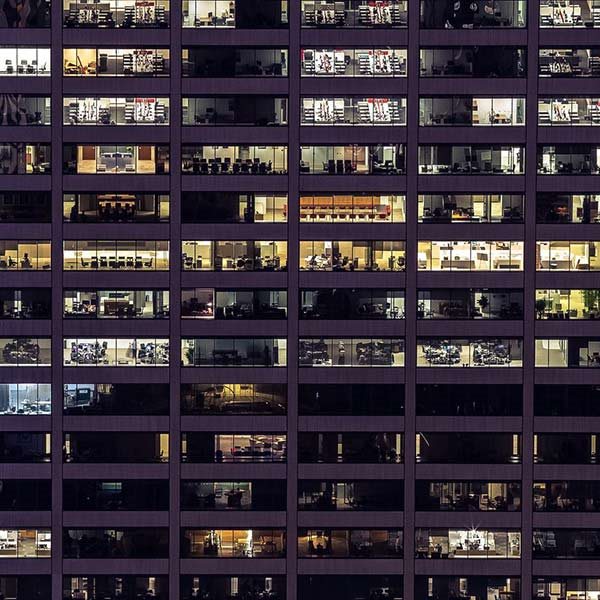 Photograph of windows in an office tower taken outside the building at night.