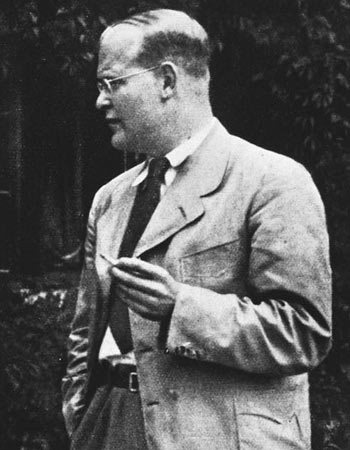 Dietrich Bonhoeffer, standing and smoking a pipe.
