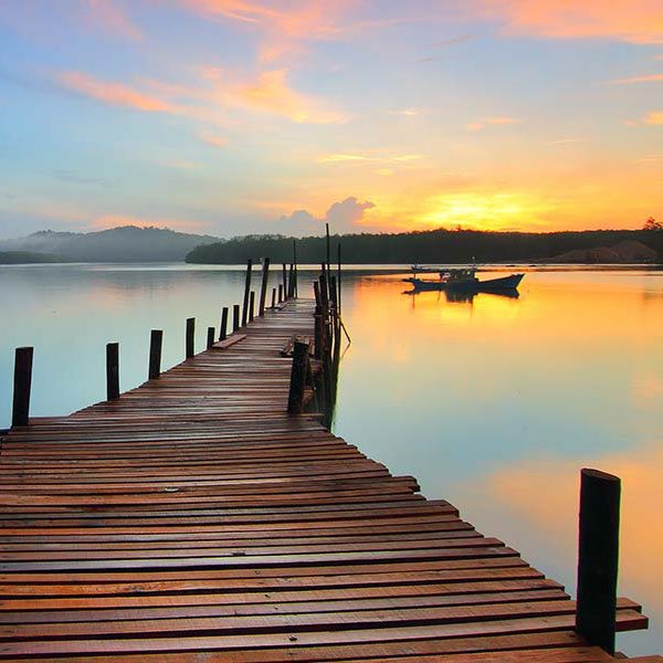 a wooden dock over a blue lake with a sunset