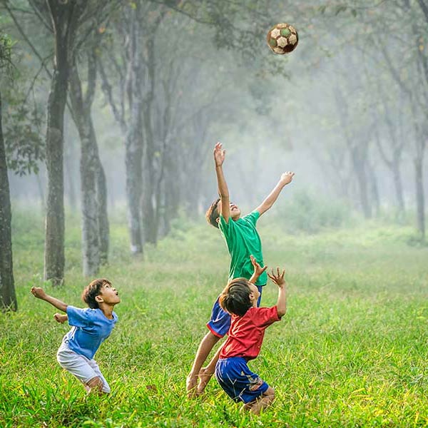 two boys jumping to hit a soccer ball in a forest
