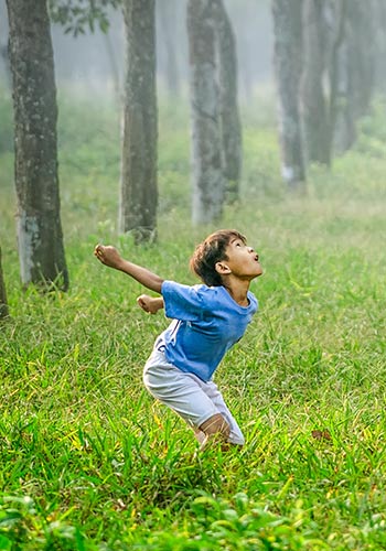 a boy jumping to hit a soccer ball in a forest