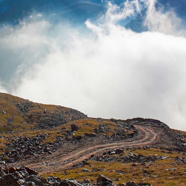 a rocky path going over a hill into mist with blue mountains behind