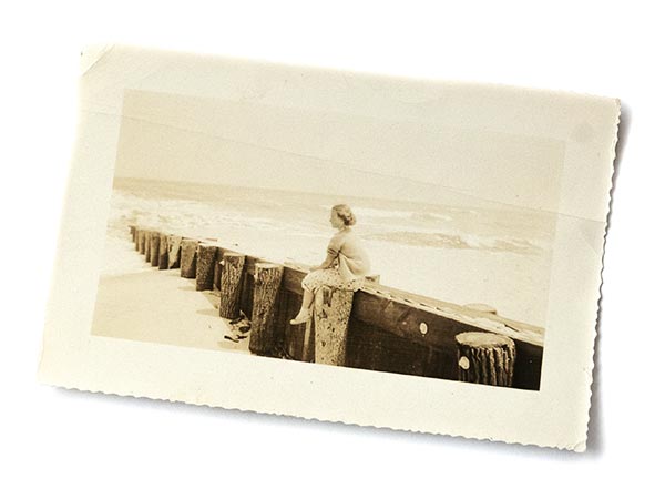 old photo of a young woman sitting on a sea wall looking at the ocean
