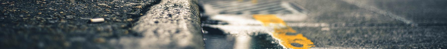 A closeup view of a sidewalk and street, near a puddle of water.