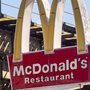 A McDonalds sign on a city street near elevated train tracks.