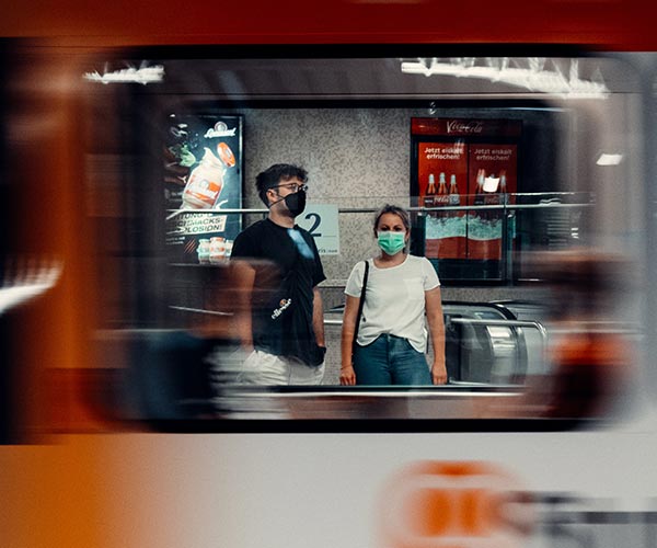 man and woman wearing masks seen through a train window
