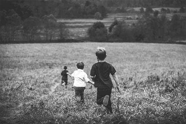 three boys running down a grassy hill