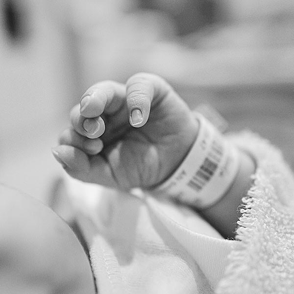 black and white photo of a babys hand with a hospital bracelet