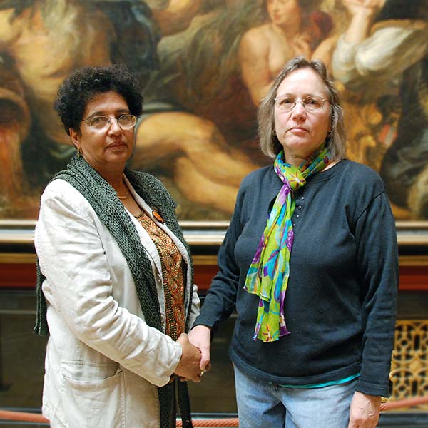 two women shaking hands in front of a painting