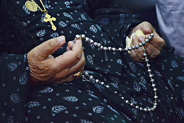 photo of an older woman holding a string of silver rosary beads