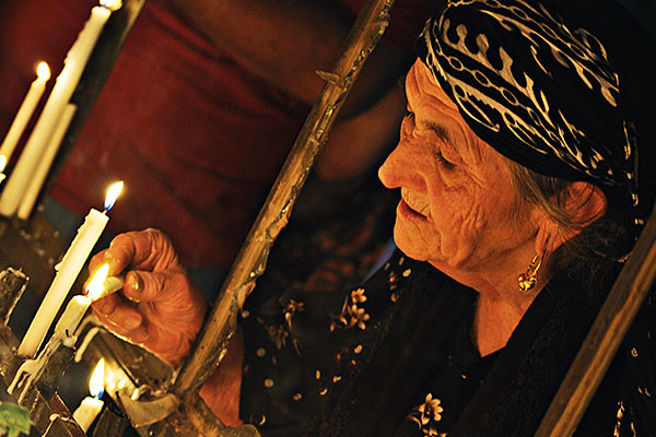 photo of an older woman in a headscarf lighting white taper candles