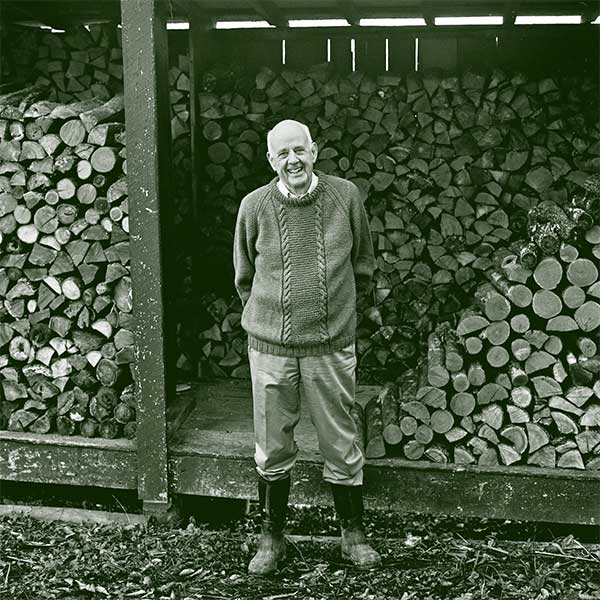photo of Wendell Berry standing in front of a pile of split wood