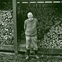 photo of Wendell Berry standing in front of a pile of split wood