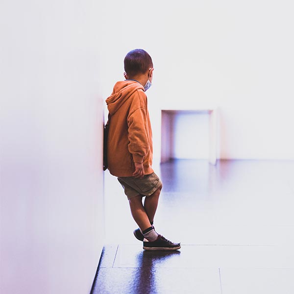 boy in an orange hoodie standing in a white hallway