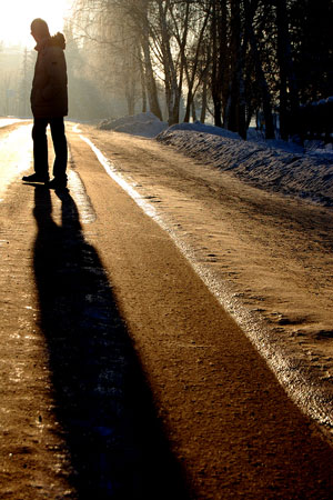 Man in a coat walking away down the road lit by evening light.