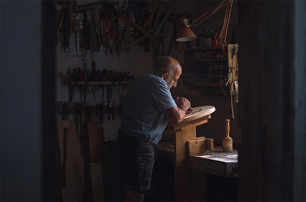 old man chiseling in a dim woodshop