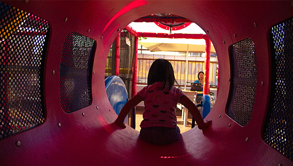 child playing in fast food restaurant playground with her mom in the background
