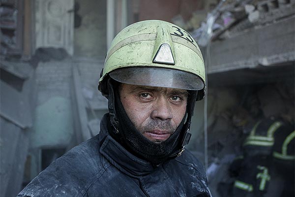 exhausted-looking man in a firefighters hat among rubble
