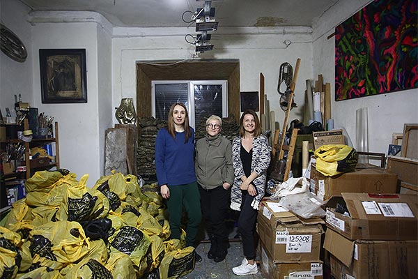 three women standing among bags and boxes