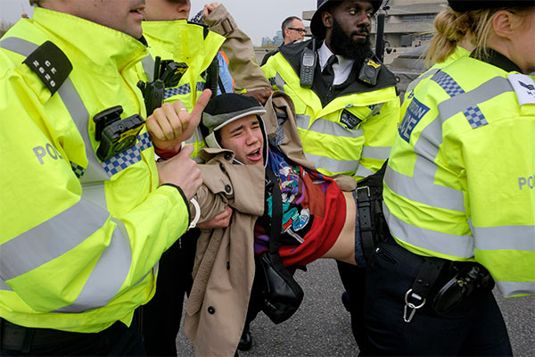 young man protesting for Extinction Rebellion being carried by London police officers in bright yellow jackets