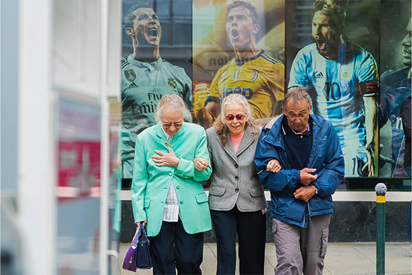 Three elderly people linking arms while walking