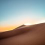 the sun rising over a sand dune