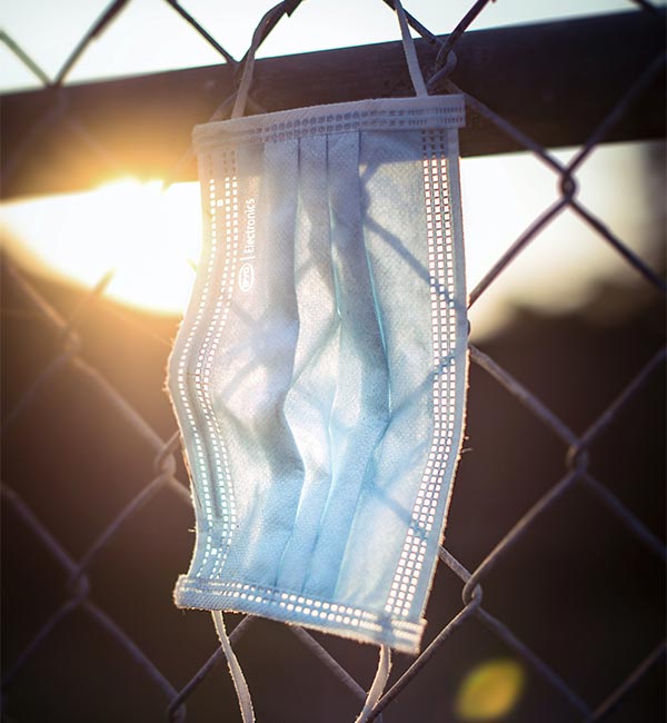 blue disposable mask hanging on a chain link fence