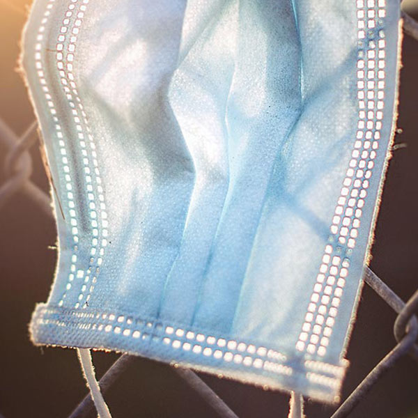 blue disposable mask hanging on a chain link fence
