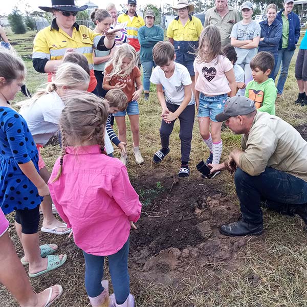 man planting a tree with a group of children watching