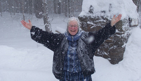 An elderly woman standing in the snow with arms outspread