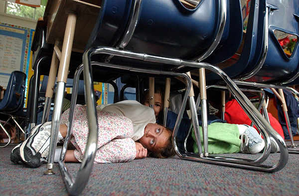 a girl curls up under her desk during a lockdown drill