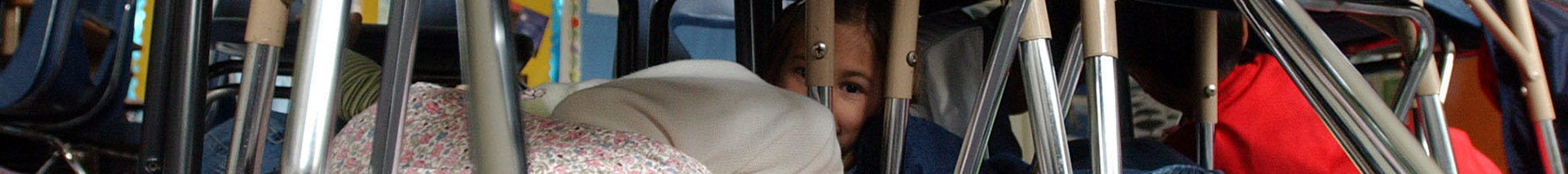 a girl curls up under her desk during a lockdown drill