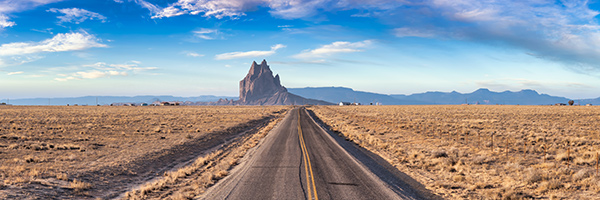 road in a dry desert with a Shiprock mountain peak in the background