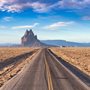 road in a dry desert with a Shiprock mountain peak in the background