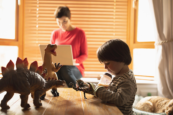 Boy playing with toys while mother uses laptop