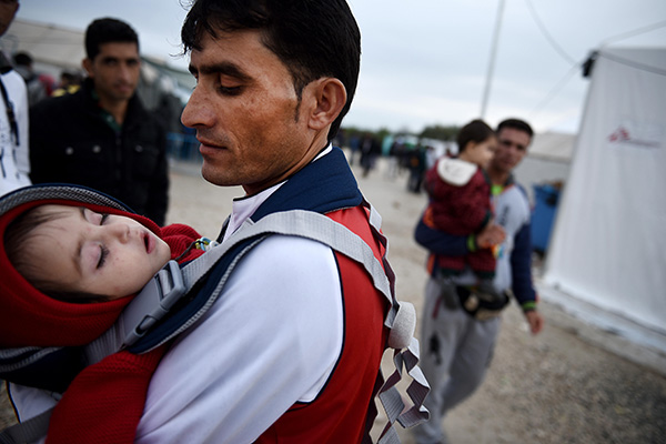 refugee man carries his child inside the makeshift refugee camp of Idomeni in norhern Greece.