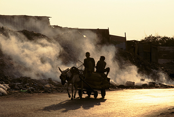 children ride a donkey cart past burning garbage