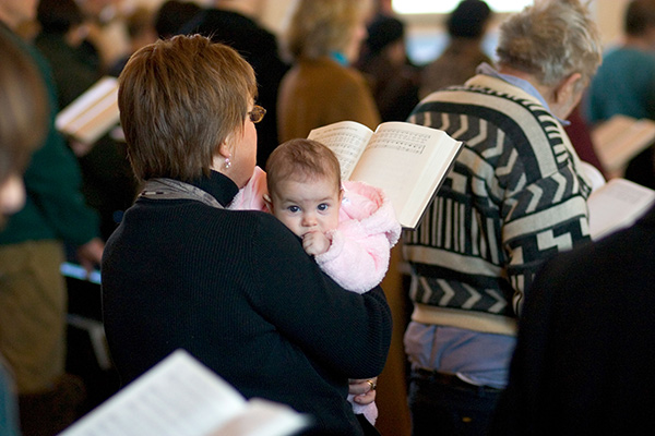 a woman holding a baby and singing from a hymnbook in a church