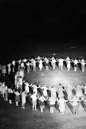 A black and white photograph showing a large group of people standing in a circle.