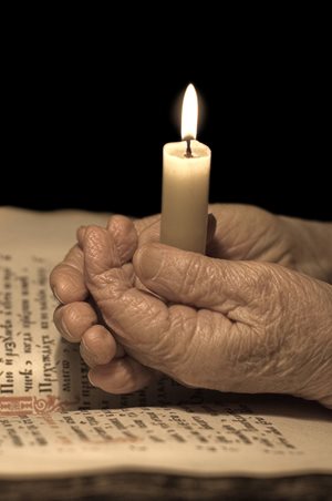 elderly hands holding a candle by a bible