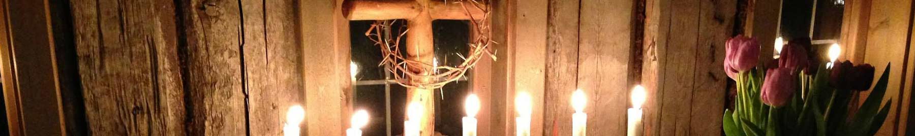 White candles burning before a wooden cross with a wreath of thorns.
