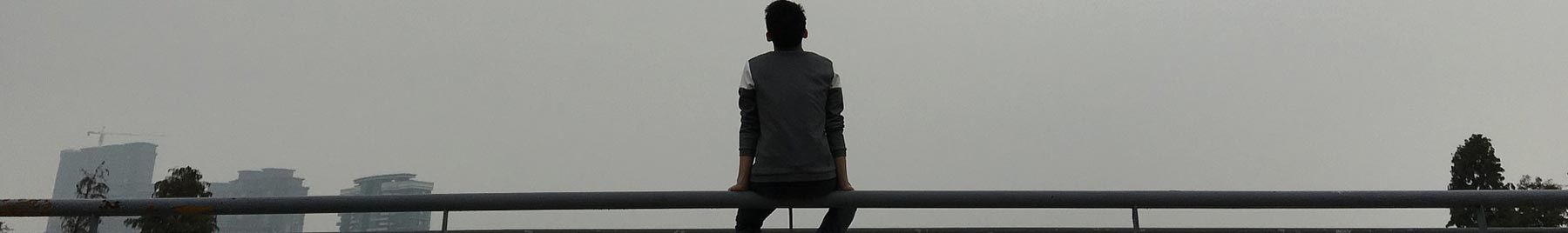 A lonely teenager sits on a bridge railing and looks at the rainy city