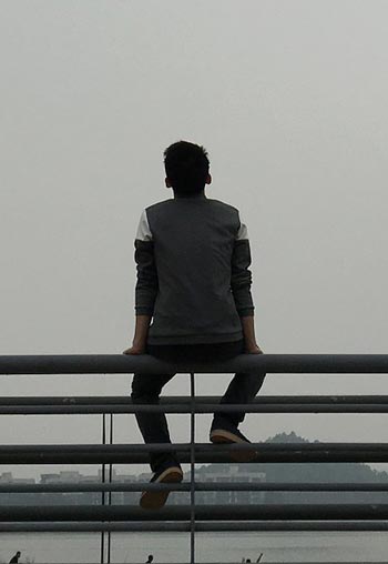 A lonely teenager sits on a bridge railing and looks at the rainy city